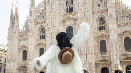 Téléchargez les photos : Attrait milanais : Une jeune femme rayonnante en manteau de fourrure blanche profite des sites touristiques de Milan, posant élégamment près de l'emblématique cathédrale de Milan. - en image libre de droit