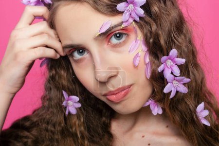 Téléchargez les photos : Élégance éthéré : les serrures bouclées d'une fille ornées de fleurs violettes dégagent grâce et sophistication, ajoutant une touche de fantaisie à son allure - en image libre de droit