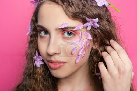 Foto de Elegantes rizos entrelazados con preciosas flores moradas, enmarcando el rostro de una encantadora joven de una manera natural y encantadora. - Imagen libre de derechos