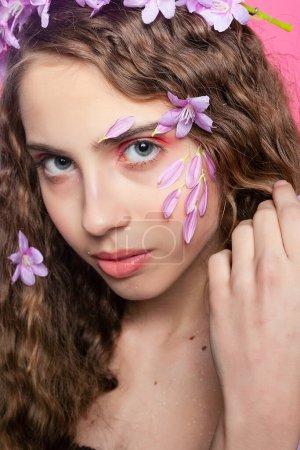 Téléchargez les photos : Boucles rayonnantes entrelacées de délicates fleurs violettes créent une couronne étonnante pour cette fille, exsudant grâce et féminité - en image libre de droit