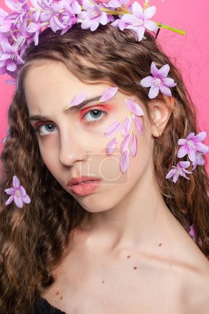 Eine Vision von Weiblichkeit: Lockiges Mädchen verschönert ihre Locken mit lila Blüten, die Eleganz und botanischen Charme ausstrahlen