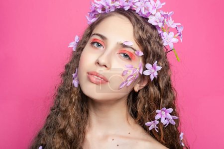 Ein fesselnder Anblick: Mädchen mit lockigem Haar präsentiert lila Blüten, die ihrem Look einen Sinn für Skurrilität und botanischen Reiz verleihen