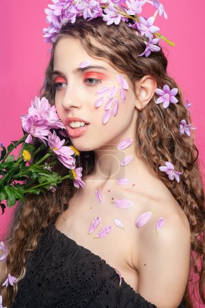 Téléchargez les photos : Beauté naturelle : Ornés de fleurs violettes, les cheveux bouclés de la jeune fille crée une vue captivante et enchanteresse, incarnant une allure florale - en image libre de droit
