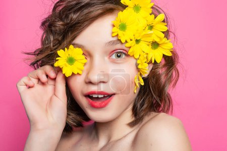Photo for Alluring image of a girl with a charming smile, her face partly covered by a yellow flower against a backdrop of pale pink. Great for conveying innocence and sweetness. - Royalty Free Image