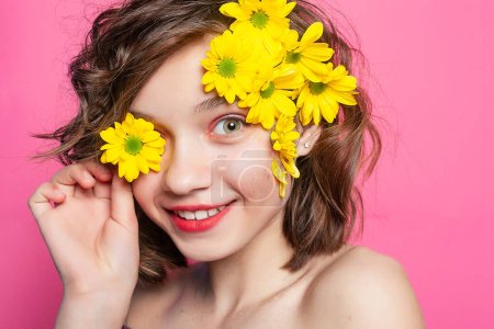 Téléchargez les photos : Image captivante d'une jeune fille tenant gracieusement une fleur jaune, ajoutant une touche de mystère sur un fond rose pastel. Idéal pour les promotions sur le thème du printemps. - en image libre de droit