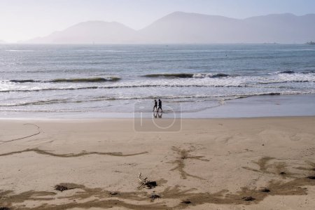 Téléchargez les photos : Couple d'amis marchant sur la plage de sable au lever du soleil pendant les vacances de printemps dans une destination paradisiaque ensoleillée. Voyage concept de vacances. Lerici, Ligurie, Italie - en image libre de droit