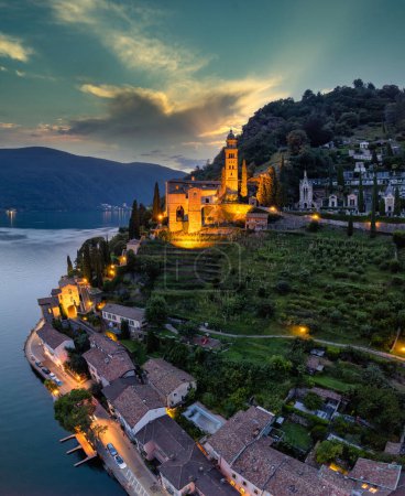 Photo for Aerial image of the parish church Madonna del Sasso stands on the high hill of Vico Morcote at sunset. Morcote at the Lake Lugano was once credited as one of the most beautiful Swiss villages. - Royalty Free Image