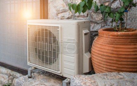 Air heat pump outdoor unit against wall of Greek house.