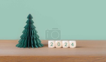 Téléchargez les photos : Cubes en bois avec numéro d'année 2024 et sapin de Noël en papier sur fond vert. - en image libre de droit