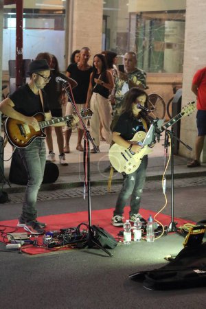 Photo for Ferrara, Italia - August 26, 2022: The Ferrara Buskers Festival is dedicated to the art of the street. The Father&Son duo plays classic rock music, a stomp box, harmonica, acoustic and electric guitar. - Royalty Free Image