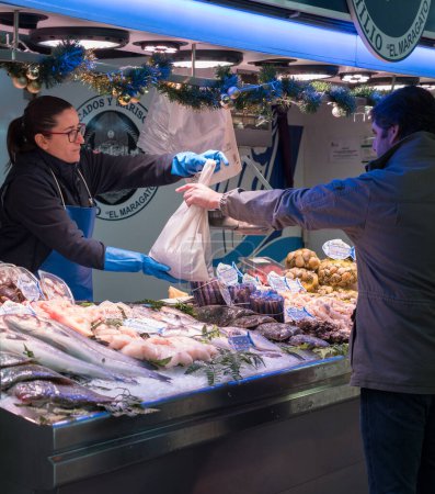 Foto de Fishmonger delivers a bag of fresh fish to a customer in a traditional market. Customers at a fish stall. Fishmonger charges a customer. - Imagen libre de derechos