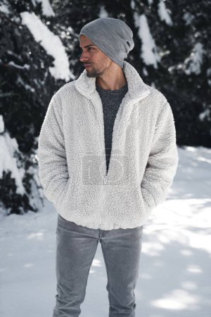 Stylish man in winter fashion outfit posing in snow