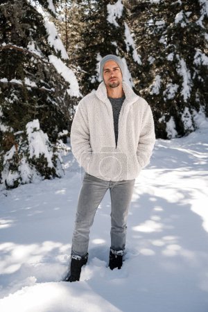 Stylish man in winter fashion outfit posing in snow