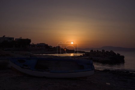 Amazing sunset on the Mediterranean Sea, view of Athens from the island of Aegina. Salty beach and a boat on the shore.