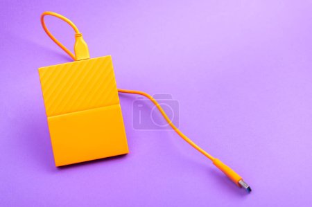 Foto de Unidades de disco duro portátiles externas de color naranja aisladas sobre fondo púrpura claro - Imagen libre de derechos