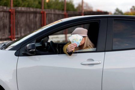 Photo for Elegant woman hides her face behind euro banknotes in the car window - Royalty Free Image