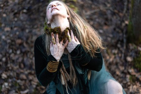 Eine Schamanin führt ein Naturritual durch, indem sie ihr Gesicht mit Waldmoos und Erde beschmiert