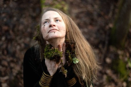 Schamanin führt ein Naturritual durch, indem sie ihr Gesicht mit Waldmoos und Erde beschmiert
