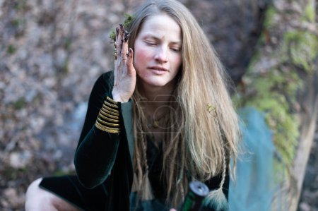 A female shaman performs a nature ritual by smearing her face with forest moss and earth