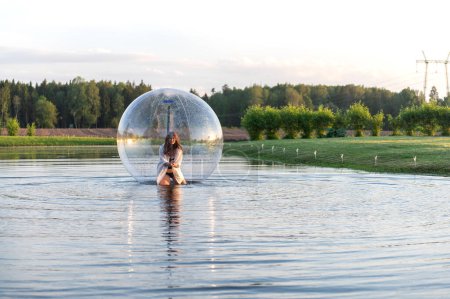 Water ball (similar to zorb or Human Hamster Ball) with young woman inside on pond surface
