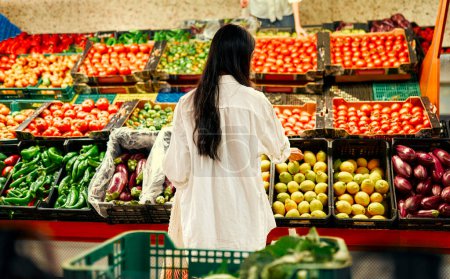 Photo for Young pretty asian woman in white shirt choosing groceries in fresh vegetables and fruits store. Healthy food concept. - Royalty Free Image