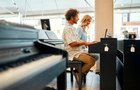 Foto de Pareja joven sentada al piano y tocando cuatro manos en una tienda de instrumentos musicales. Pasatiempos y recreación. Comprar un piano en una tienda. - Imagen libre de derechos