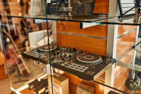 Foto de Close-up of a DJ controller on a glass shelf in a musical instrument store. Lots of different musical instruments for sale. Hobbies and recreation. - Imagen libre de derechos