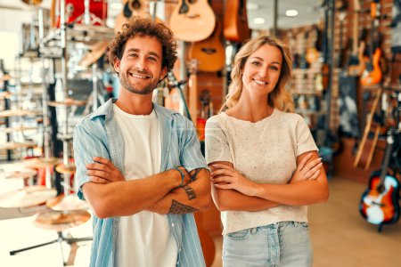 Foto de Sales consultants standing in a musical instrument store against the backdrop of walls with many different guitars. Buying a guitar and musical instruments. - Imagen libre de derechos