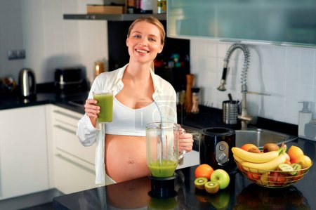 Photo for A young pregnant woman is preparing a smoothie with a blender in the kitchen. A pregnant woman drinks a vitamin smoothie. The concept of healthy eating during pregnancy. - Royalty Free Image