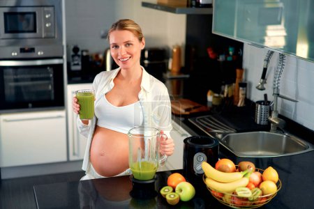Foto de Una joven embarazada está preparando un batido con una licuadora en la cocina. Una mujer embarazada bebe un batido de vitaminas. El concepto de alimentación saludable durante el embarazo. - Imagen libre de derechos