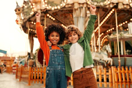 Téléchargez les photos : Une fille afro-américaine et un garçon caucasien avec une coiffure bouclée s'amusent dans un parc d'attractions et de loisirs. - en image libre de droit