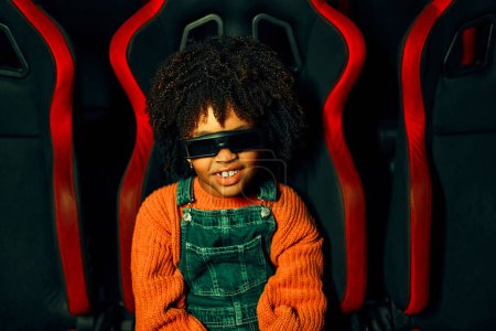 Téléchargez les photos : Une fille mignonne afro-américaine avec et un garçon caucasien mignon assis dans un cinéma virtuel à lunettes sur des chaises tournantes mobiles et regardant émotionnellement un film dans un parc d'attractions. - en image libre de droit