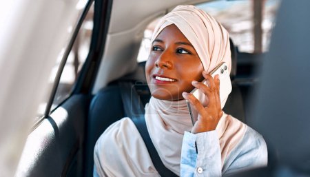 Téléchargez les photos : Jeune femme musulmane en hijab parlant au téléphone alors qu'elle était assise dans une voiture. - en image libre de droit