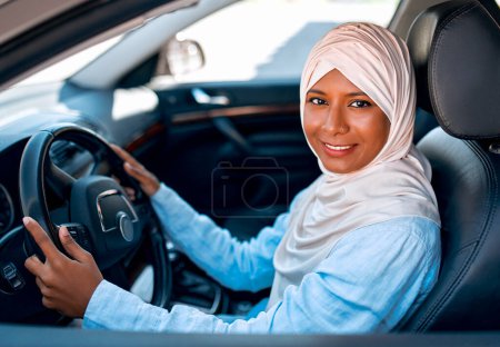 Téléchargez les photos : Jeune femme musulmane en hijab assise au volant d'une voiture. Acheter et louer une voiture. Voyages et loisirs. - en image libre de droit