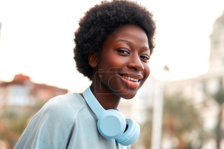 Téléchargez les photos : Femme afro-américaine écoutant de la musique dans des écouteurs avec une coiffure afro dans la rue et passer un week-end amusant. - en image libre de droit
