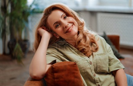Téléchargez les photos : Adulte belle femme blonde assise sur le canapé dans le salon à la maison, reposante et relaxante. - en image libre de droit