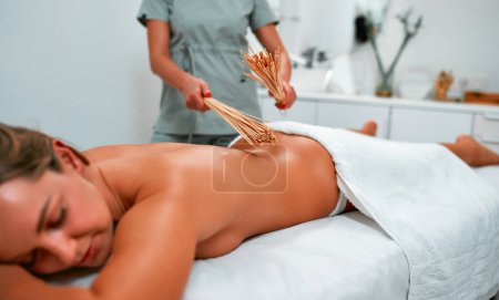 Photo for The masseur makes anti-cellulite massage in the spa with a bamboo stick, spa treatments. The concept of health and beauty. Body massage with bamboo brooms. - Royalty Free Image