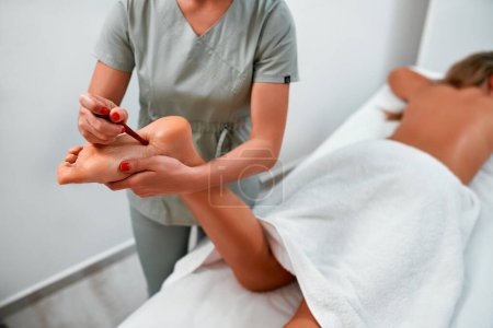 Téléchargez les photos : Femme ayant un massage relaxant avec bâton de massage des pieds dans le salon de beauté spa. Client recevant un traitement d'acupression avec un bâton de masseur en bois. Médecine naturelle, réflexologie, acupression - en image libre de droit