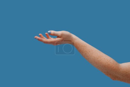 Foto de Mano femenina con pecas sosteniendo la palma hacia arriba aislada sobre fondo azul. Copiar espacio. Lugar para insertar un producto para publicidad. - Imagen libre de derechos