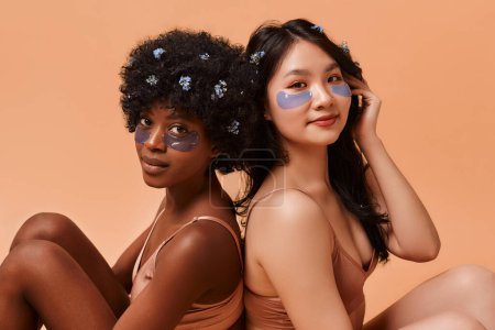 Téléchargez les photos : Jeunes femmes afro-américaines et asiatiques utilisant des bandeaux en lingerie posant sur fond beige. Cosmetologie et soins spa pour le visage et le corps. - en image libre de droit