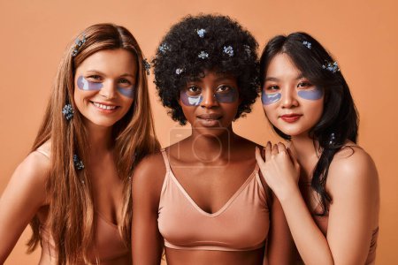 Photo for Multiethnic women in lingerie isolated on beige background using eye patches. African American, Caucasian and Asian women posing in the studio. Cosmetology and spa care. - Royalty Free Image