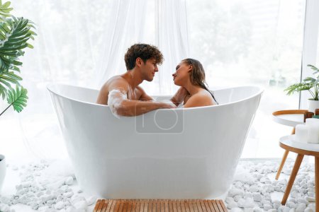 Foto de Sexy pareja joven sensual romántica abrazando y tomando un baño de burbujas. Una dama apasionada se relaja en el baño con su novio fornido. - Imagen libre de derechos