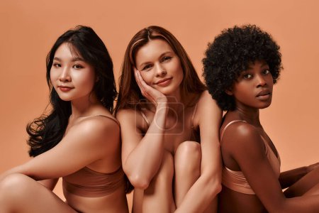Photo for Multi-ethnic multiracial young women in beige lingerie isolated on a beige background. African-American, Caucasian and Asian women posing in the studio. Concept of face body skin care, cosmetology. - Royalty Free Image