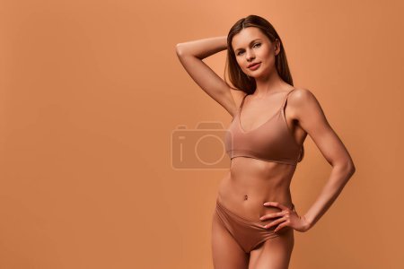 Téléchargez les photos : Belle jeune femme caucasienne mince en lingerie beige posant sur fond beige. Le concept des soins de la peau, de la cosmétologie et des soins spa. - en image libre de droit