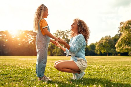 Photo for Beautiful happy young mother holding the hands of her beloved little daughter in the meadow in the park on a warm sunny day, playing and having fun together. - Royalty Free Image