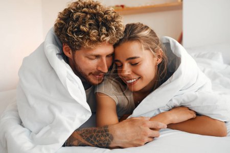 Téléchargez les photos : Jeune couple amoureux couché sur le canapé dans la chambre sous une couverture, s'amuser et profiter de l'autre le week-end. - en image libre de droit