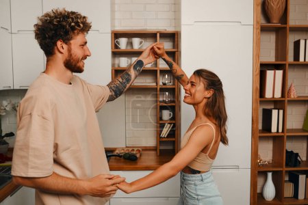 Photo for Young beautiful couple in love dancing in the kitchen, cooking breakfast, having fun together weekends. - Royalty Free Image
