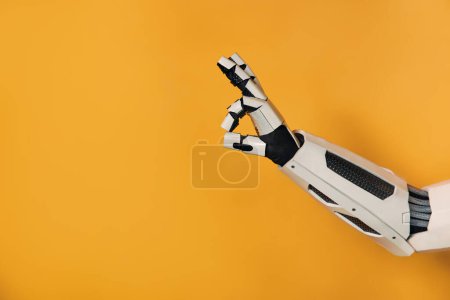 Foto de Mano robot mostrando gesto ok aislado sobre fondo naranja. Colaboración entre humanos e inteligencia artificial. - Imagen libre de derechos