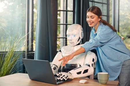 Photo for Young woman with a cup of coffee and a humanoid robot working while sitting at a laptop in a modern office. Collaboration between humans and artificial intelligence. - Royalty Free Image