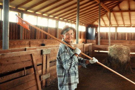 Foto de Madura hermosa mujer agricultora que trabaja con una horca en un granero en una granja. Concepto de agricultura y agricultura. - Imagen libre de derechos